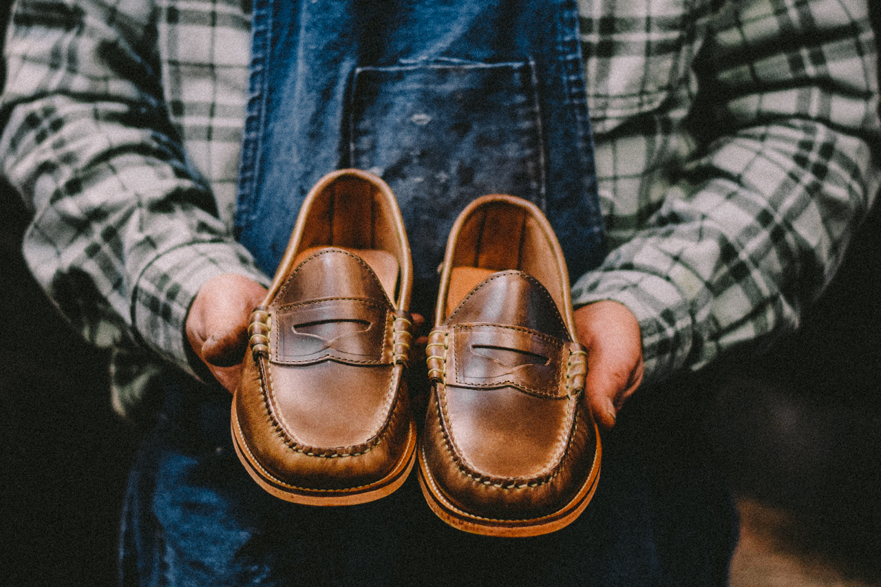 A shoemaker proudly holds a new pair of Oak Street Bootmakers hand-sewn Beefroll Penny Loafers